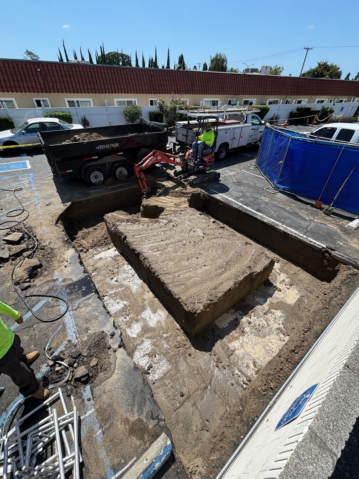 Trench cut through a parking lot with the spoils loaded for haul-off