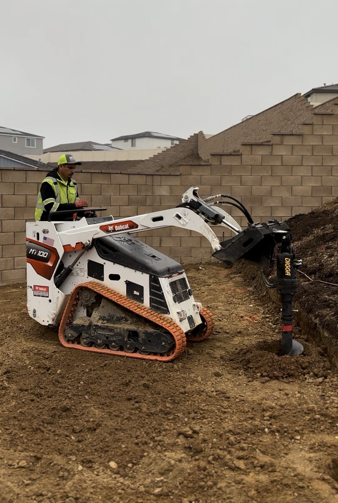 Mini track loader with auger next to a block wall